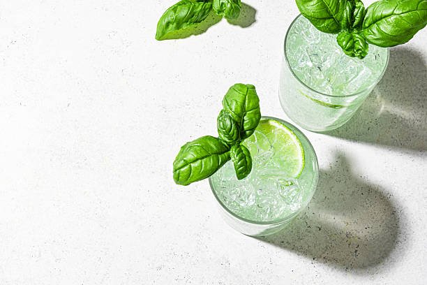 Fresh summer green cocktail drink with lime and basil on white background, top view, copy space. Ginger Gin Fiizz. Citrus and basil iced detox water.