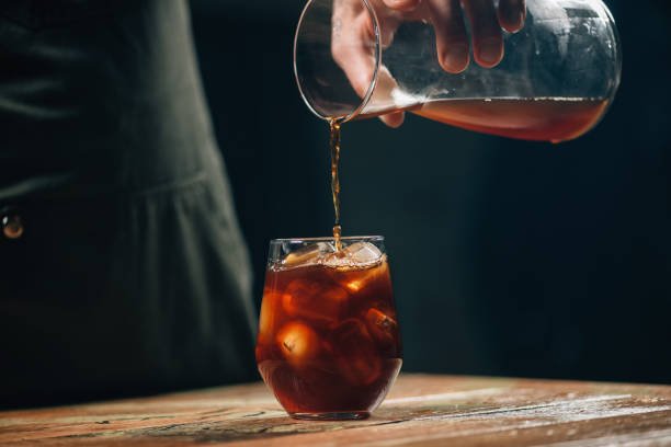 Hands of a barista pouring cold brew coffee over ice cubes