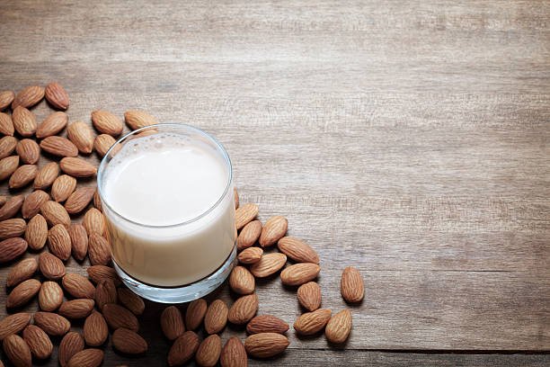 A glass of almond milk surrounded by almonds.